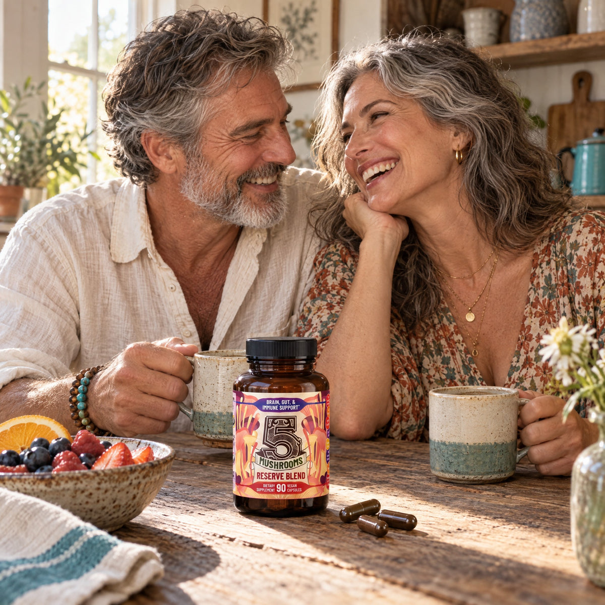 A couple laughing over two mugs of coffee at a farmhouse table with a bottle of 5 Mushrooms Reserve Blend